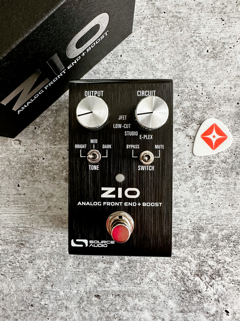 A box with a guitar and a guitar pick next to it, featuring the Source Audio ZIO Analog Front End + Boost pedal for an all-analog preamp/boost experience.